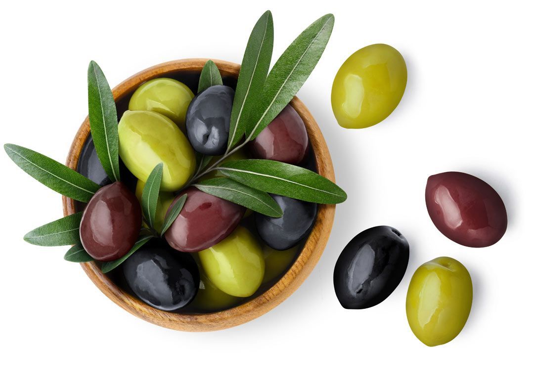 Holzschale mit grünen, schwarzen und roten Oliven, dekoriert mit Olivenzweigen, daneben einzelne Oliven.